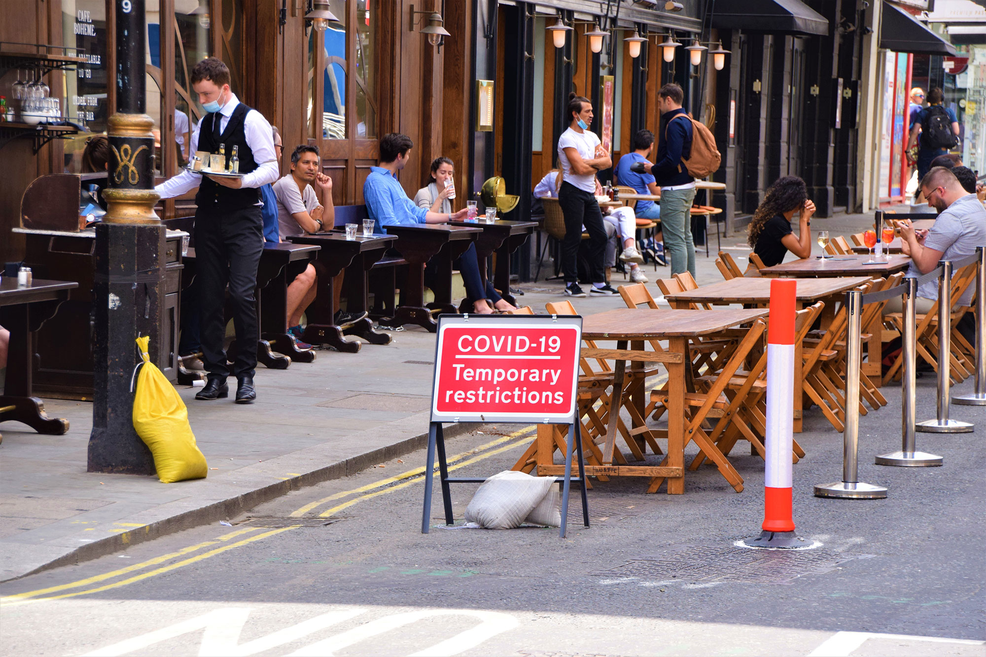 People dining outside by a sign which reads "COVID-19 temporary restrictions".